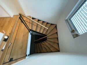 Escalier moderne bois métal type industriel avec limon en acier laqué, garde-corps en fer plat et finition main courante bois soudé et remplissage cables inox et verre en aprtie basse