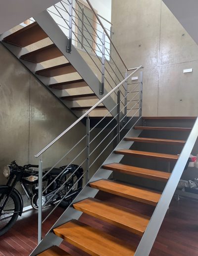 Escalier design industriel en acier gris avec marches en bois et garde-corps inox, poteaux plats et main courante ronde soudée. Escalier avec palier intérmédiaire