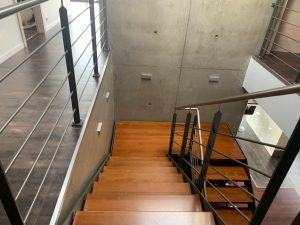 Escalier design industriel en acier gris avec marches en bois et garde-corps inox, poteaux plats et main courante ronde soudée. Escalier avec palier intérmédiaire