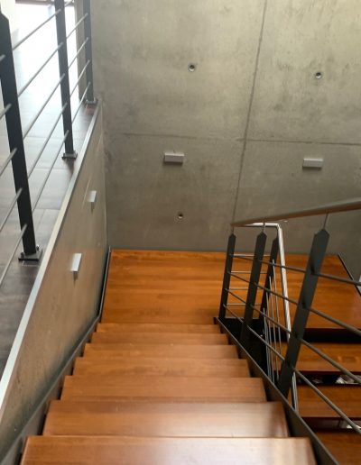 Escalier design industriel en acier gris avec marches en bois et garde-corps inox, poteaux plats et main courante ronde soudée. Escalier avec palier intérmédiaire