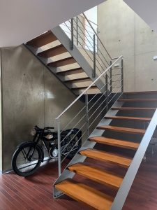 Escalier design industriel en acier gris avec marches en bois et garde-corps inox, poteaux plats et main courante ronde soudée. Escalier avec palier intérmédiaire