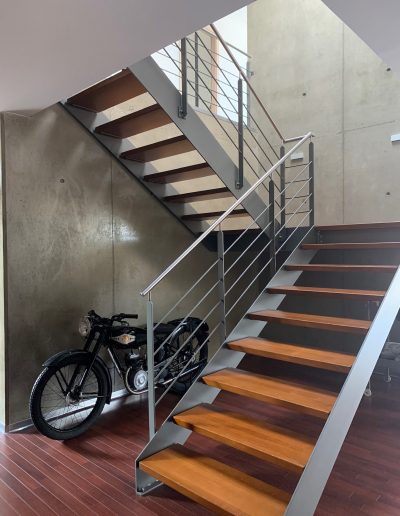 Escalier design industriel en acier gris avec marches en bois et garde-corps inox, poteaux plats et main courante ronde soudée. Escalier avec palier intérmédiaire