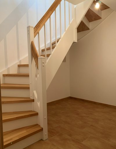 Escalier traditionnel en bois avec main courante et marches en chênes. Contre marche et limon laqué en blanc, ballustres bois