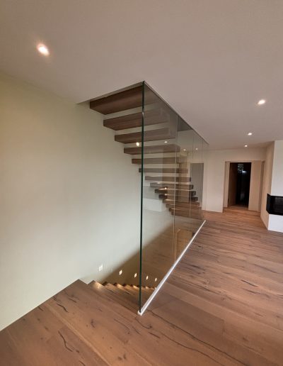Garde-corps horizontal et rampant en full verre sans poteau apparant autour d'un escalier suspendu autoporteur design en bois