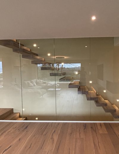 Garde-corps horizontal et rampant en full verre sans poteau apparant autour d'un escalier suspendu autoporteur design en bois
