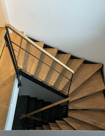 Escalier moderne bois métal type industriel avec limon en acier laqué, garde-corps en fer plat et finition main courante bois soudé et remplissage cables inox et verre en aprtie basse