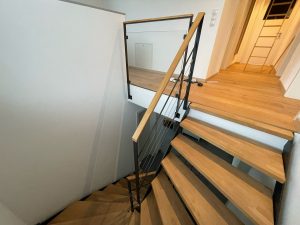 Escalier moderne bois métal type industriel avec limon en acier laqué, garde-corps en fer plat et finition main courante bois soudé et remplissage cables inox et verre en aprtie basse