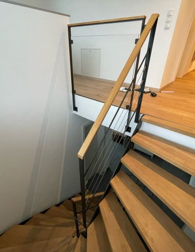Escalier moderne bois métal type industriel avec limon en acier laqué, garde-corps en fer plat et finition main courante bois soudé et remplissage cables inox et verre en aprtie basse