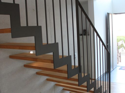 Escalier design à Dettwiller : limon crémaillère en acier gris marche aboutée en chêne et garde-corps en acie rplat avec barreaudage verticale laqué gris
